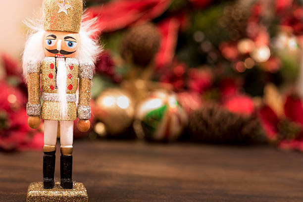 Close-up view of an elegant gold Christmas nutcracker ornament on wooden table with many red, gold and green decorations or Christmas tree in background.  Copyspace at side.  NOTE:  This image created for the Getty Creative Content Brief #663372617.   This ornament is not original artwork.