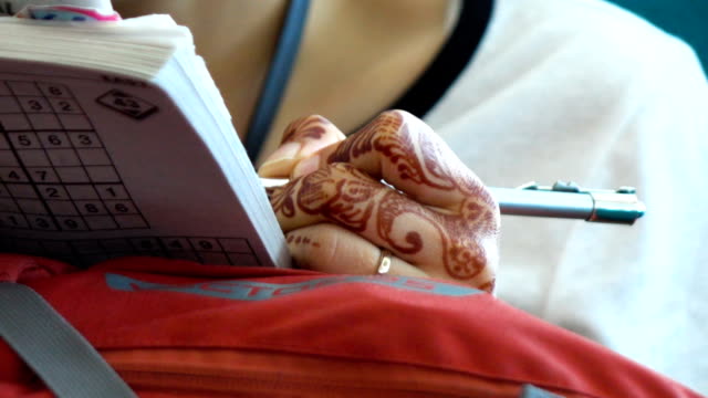 Girl with hands painted Mehndi playing a sudoku puzzle