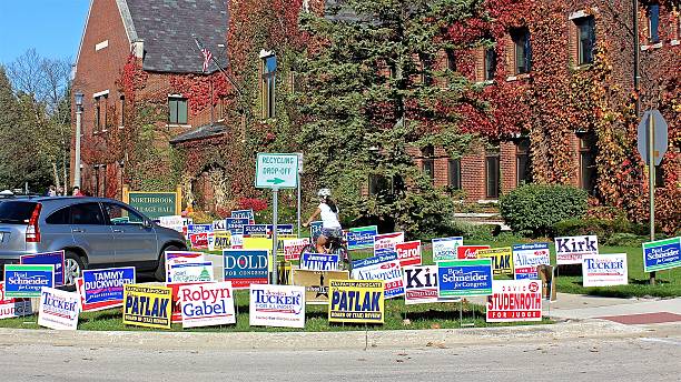 Biker riding through election political lawn signs outside polling place Northbrook, IL, USA - November 6, 2016: Biker riding on sidewalk through election campaign political lawn signs for local, state and national candidates outside polling place during early voting at Village Hall.  yard sign stock pictures, royalty-free photos & images