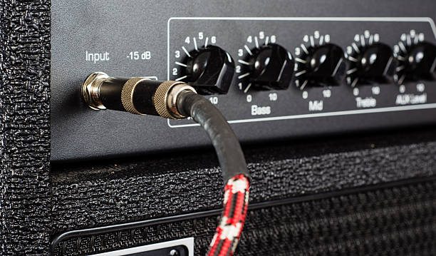 Plugged In Close up of a red braided cord plugged into the input of a bass guitar amplifier. amplifier plug stock pictures, royalty-free photos & images