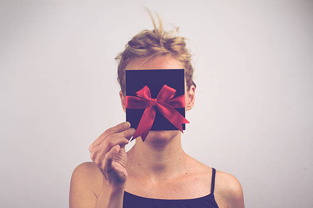 Young blonde woman holding a card with ribbon in front Portrait of a young Caucasian woman holding a black gift card with red ribbon in front of her face red blindfold stock pictures, royalty-free photos & images