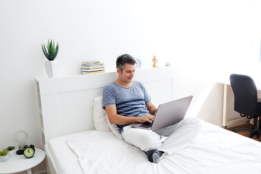 Beautiful young man using laptop while sitting on a bed