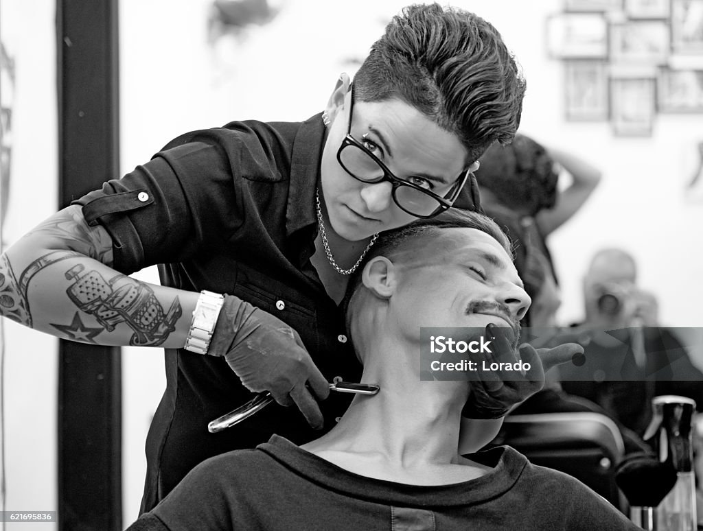 Female barber tattooed woman styling attractive threatening moustachioed male victim Barber Stock Photo