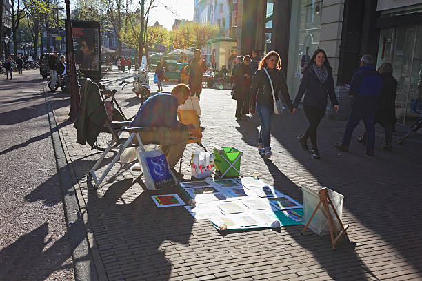 Amsterdam, Netherlands - May 1, 2016: People walking and shopping. Street artists painting tourists' portraits, Amsterdam, Netherlands
