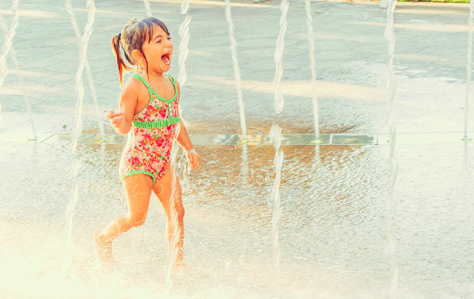 Happy little girl runs through a splashpad having fun