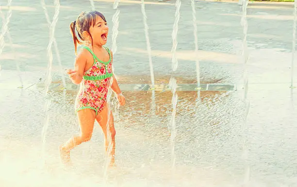 Happy little girl runs through a splashpad having fun