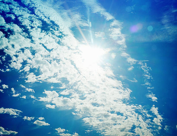 Looking up at the sun, behind a floating bank of cirro-cumulus clouds, in a  bright blue sky. Beautiful natural background.