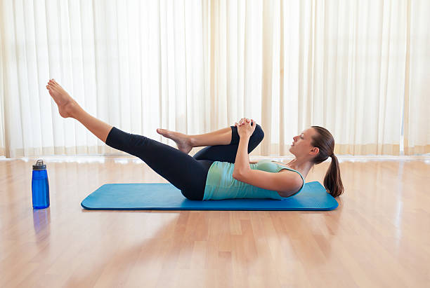 Pilates exercising Young female doing lie down leg stretches. hand on knee stock pictures, royalty-free photos & images