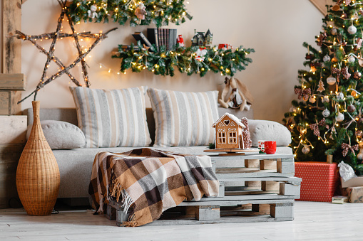 Calm image of interior modern home living room decorated christmas tree and gifts, sofa, table covered with blanket