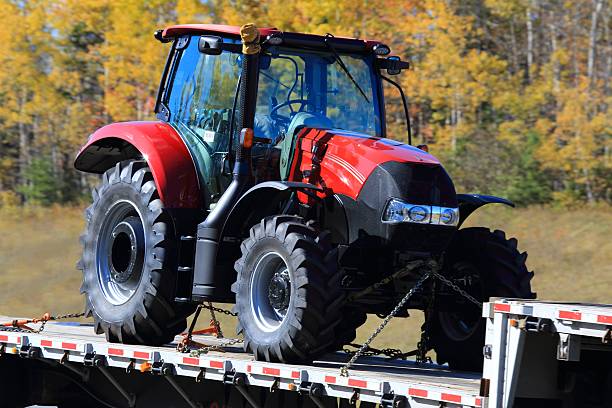 istock New tractor on a flatbed trailer, trees in the background. 621705792
