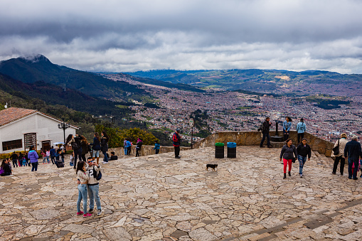 Bogota, Colombia - June 29, 2016: Colombian tourists enjoy the view and snap away on their cell phones on the Andean peak of Monserrate in Bogota, the capital city of Colombia, South America. Some admire the view. The young couple in the foreground are busy shooting a selfie. The elevation is over 10,300 feet above mean sea level. About 1,500 feet down below, is the city, which is also part of the Altiplano Cundiboyacense. Photo shot in the morning sunlight on an overcast day. Horizontal format.