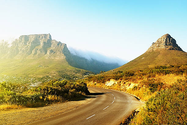 The scenic road to Table Mountain A winding road runs beside Lions Head and towards Cape Town's Table Mountain on a clear sunny day. The "Tablecloth" can be seen pouring over the face of Table Mountain. lions head mountain stock pictures, royalty-free photos & images