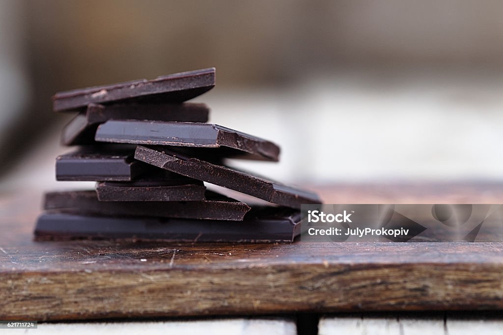 Stack of broken chocolate bar pieces Stack of broken dark chocolate bar pieces on a wooden background. Horizontal Dark Chocolate Stock Photo