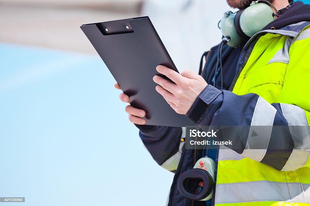 Ground crew in front of airplane Aircraft engineer holding clipboard in hands standing outdoor in front of airplane. Unrecognizable person. Air Vehicle Stock Photo