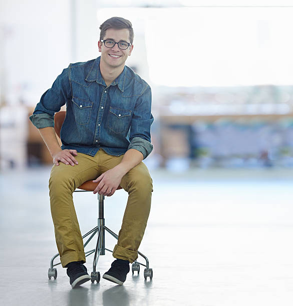 I don't need a desk to excel! Portrait of a smiling young designer sitting on a chair in a large office office chair stock pictures, royalty-free photos & images