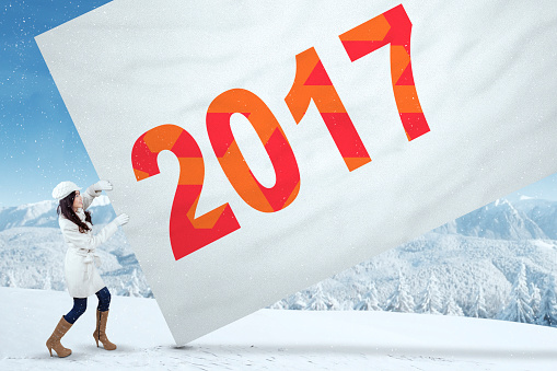 Teenage girl pulling a big banner with number 2017, shot outdoors on the snow mountain view