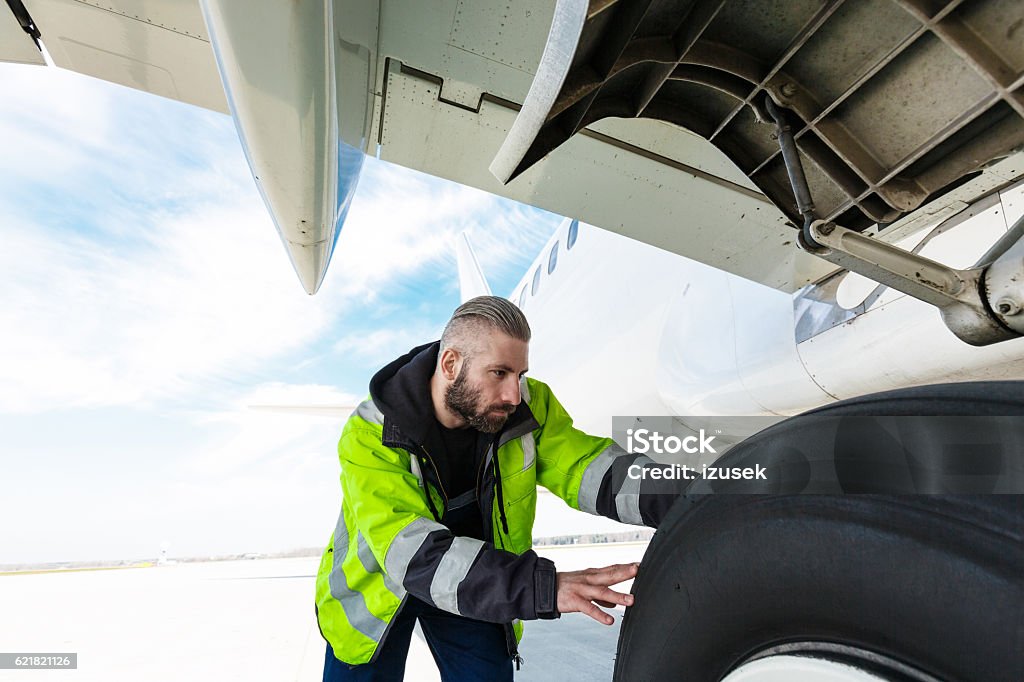 Airport worker checking tires Airport worker chcecking aircraft chassis. Ground Crew Stock Photo