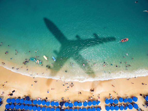 flugzeugschatten über einem überfüllten strand - travel to mexico stock-fotos und bilder