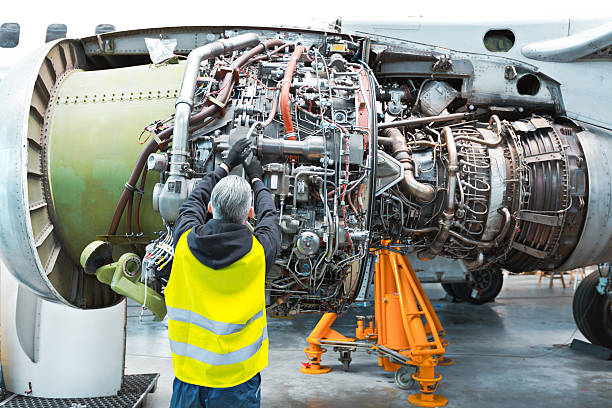 Back view of aircraft mechnic repairing jet engine in a hangar.