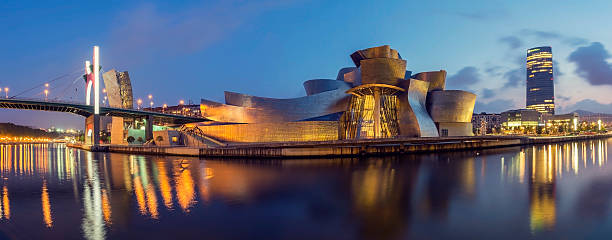 Guggenheim Museum Bilbao and Iberdrola Tower at dusk Bilbao, Spain - September 5, 2012: Panoramic view of La Salve Bridge, Guggenheim Museum and Iberdrola Tower on the bank of Nervion river in Bilbao at dusk. frank gehry building stock pictures, royalty-free photos & images