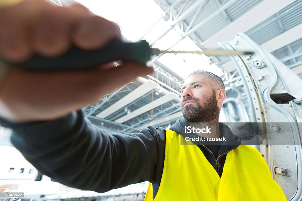 Aircraft mechnic repairing airplane in a hangar Aircraft mechnic holding screwdriver and repairing airplane in a hangar. Adult Stock Photo