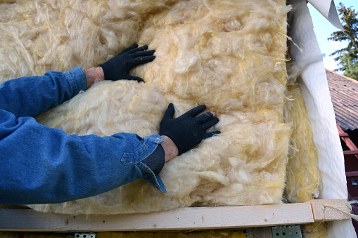 Builder hands wearing glove insulating wooden house with mineral  wool