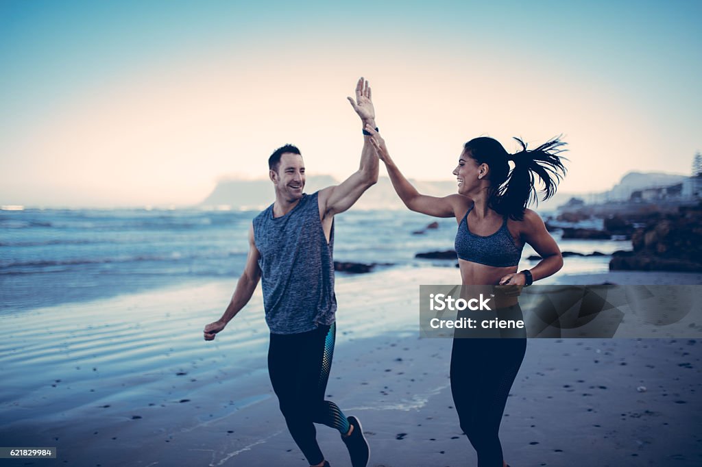 Fitness Couple giving each other high five after hard training Fitness Couple giving each other high five after hard training session on the beach Couple - Relationship Stock Photo