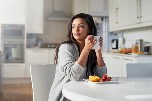 Shot of young woman daydreaming while enjoying breakfast in her kitchen at home