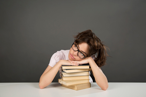 Cute, caucasian, nerd girl sitting at the desk and leaning on a stack of books