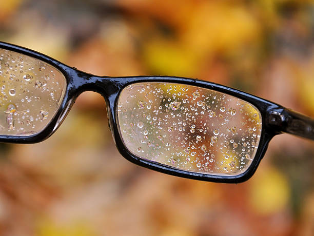 Glasses in a black frame with raindrops on the lens.