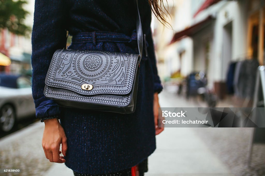 Young woman street style leather purse and a coat Close up on the young woman's purse and a dark coat on the streets of Berlin, in Kreuzberg - Schoneberg district. Vintage color graded, shot with large aperture lens for smooth and creamy bokeh background. Purse Stock Photo