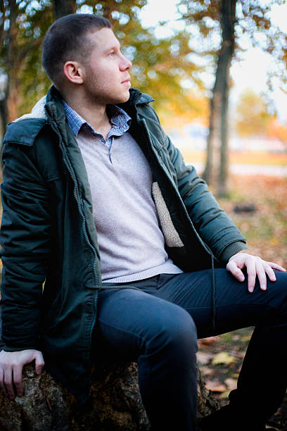 istock Young beautiful man in autumn park sitting on stump 621840786
