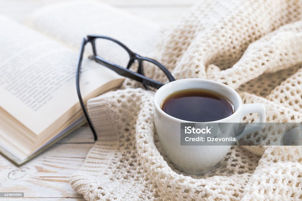 Warm knitted plaid, glasses, cup of hot coffee and book Warm knitted plaid, glasses, cup of hot coffee and book on wooden table. Autumn and winter, leisure concept Coffee - Drink Stock Photo