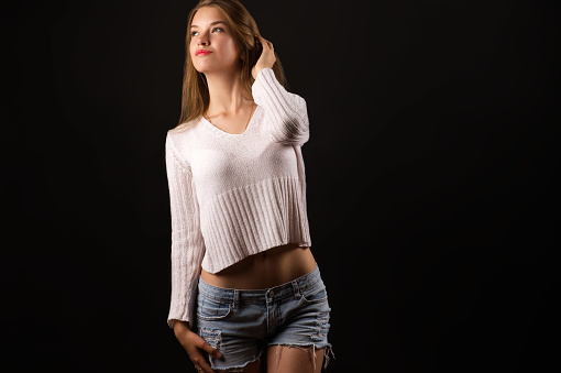 charming blonde teenager girl in white sweater isolated on black background