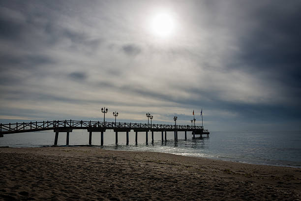 Silhouette of an old wooden jetty entering the sea on a beach in Marbella against a dramatic sky.
