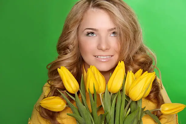 Happy smiling girl with spring-flower yellow tulips isolated on green background