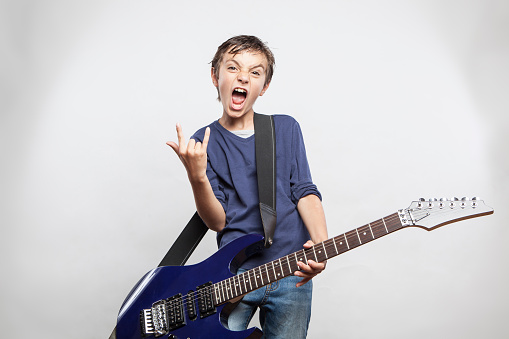 Portrait of adorable young boy playing electric guitar. kid shows the rock and roll gesture