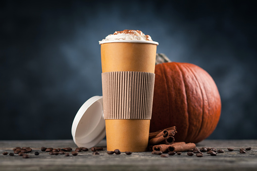 Pumpkin spice latte in a paper cup on dark background