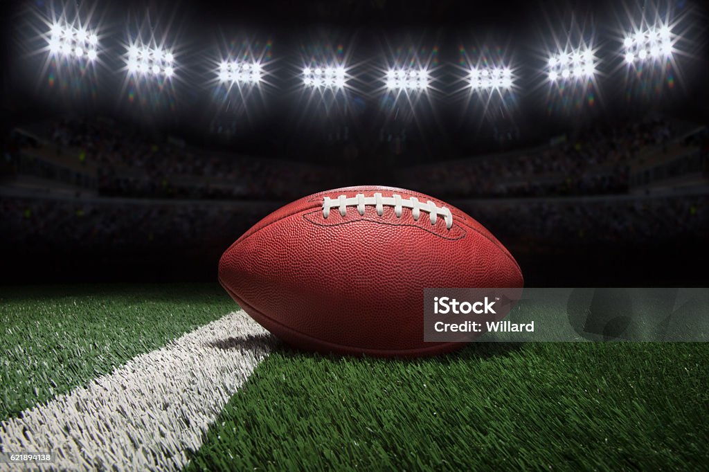 Professional style football on field with stripe under stadium lights Low angle view of professional style football on yard line of field under stadium lights American Football - Sport Stock Photo