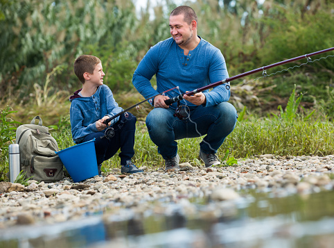 Happy father and boy fishing with rods in summer day
