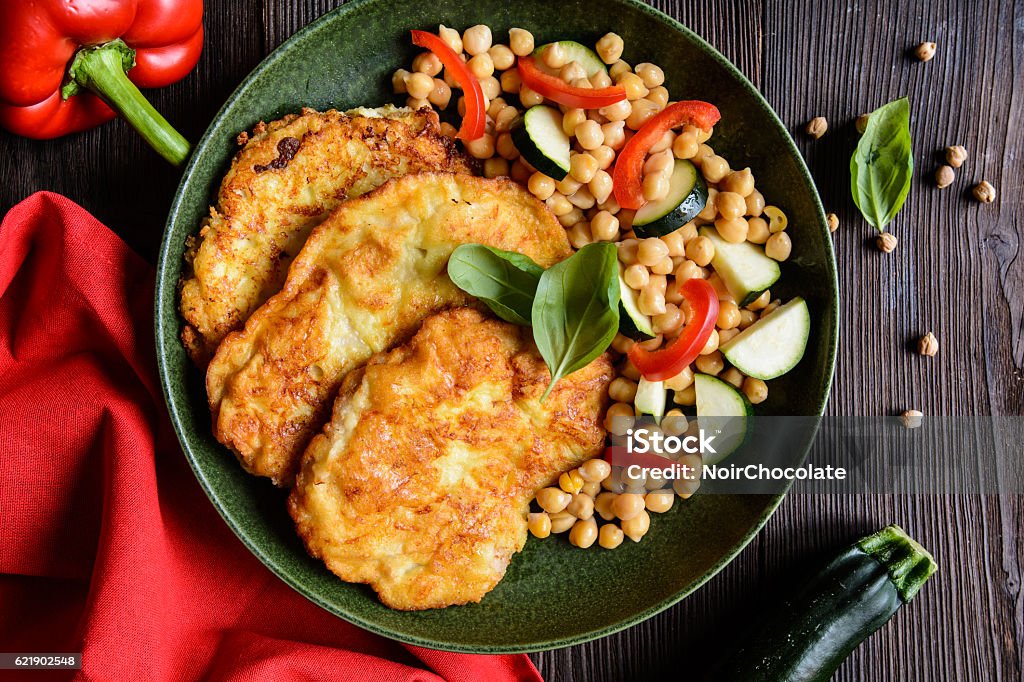 Roasted pork cutlets coated in cheese and breadcrumbs Roasted pork cutlets coated in cheese and breadcrumbs, garnished with chick peas, pepper and zucchini Breaded Stock Photo