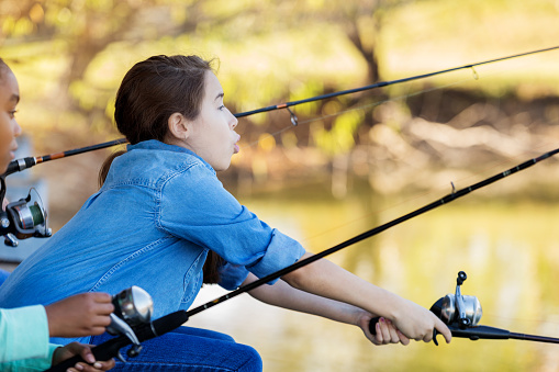 A little girl stands with a fishing rod and catches fish on the river on a summer day