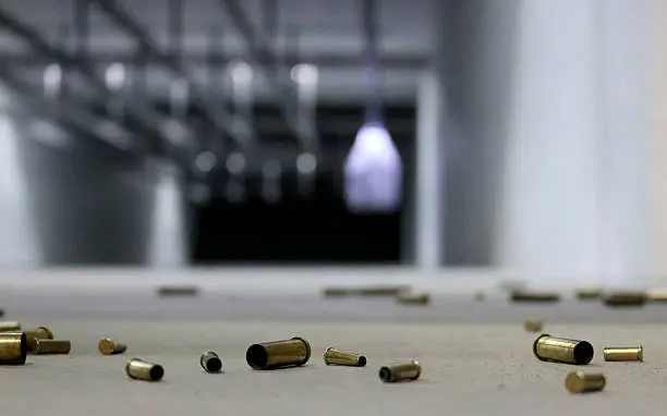 A variety of different shell casings spread across the floor at a shooting range with target in the background.