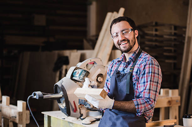 istock Handsome carpenter in protective glasses is looking at camera and 621910640