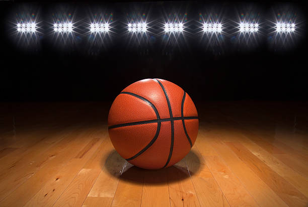 Basketball on wood floor beneath bright lights