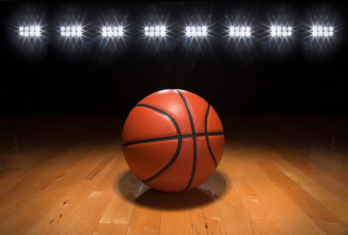 A basketball on a wood floor beneath bright arena lights