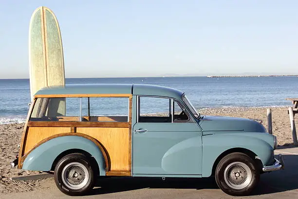 A woody station wagon at the beach with a surfboard behind it.