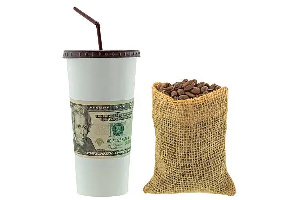 White paper cup wrapped with USD dollar banknote money next to a hemp sack of roasted coffee beans isolated on white background