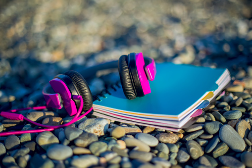 Pink headphones lying at paper notebook on sea beach. Closeup. Work and lifestyle concept. Freelancer. Musiic listening, Travel.