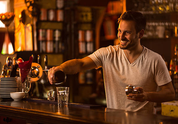 Happy bartender at bar counter preparing a cocktail. Young smiling barista at bar counter pouring cocktail  into a glass. cocktail shaker photos stock pictures, royalty-free photos & images